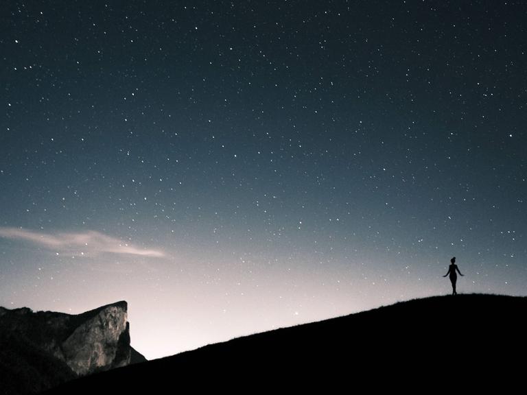 Silhouette einer Frau unter einem Sternenhimmel in den Bergen