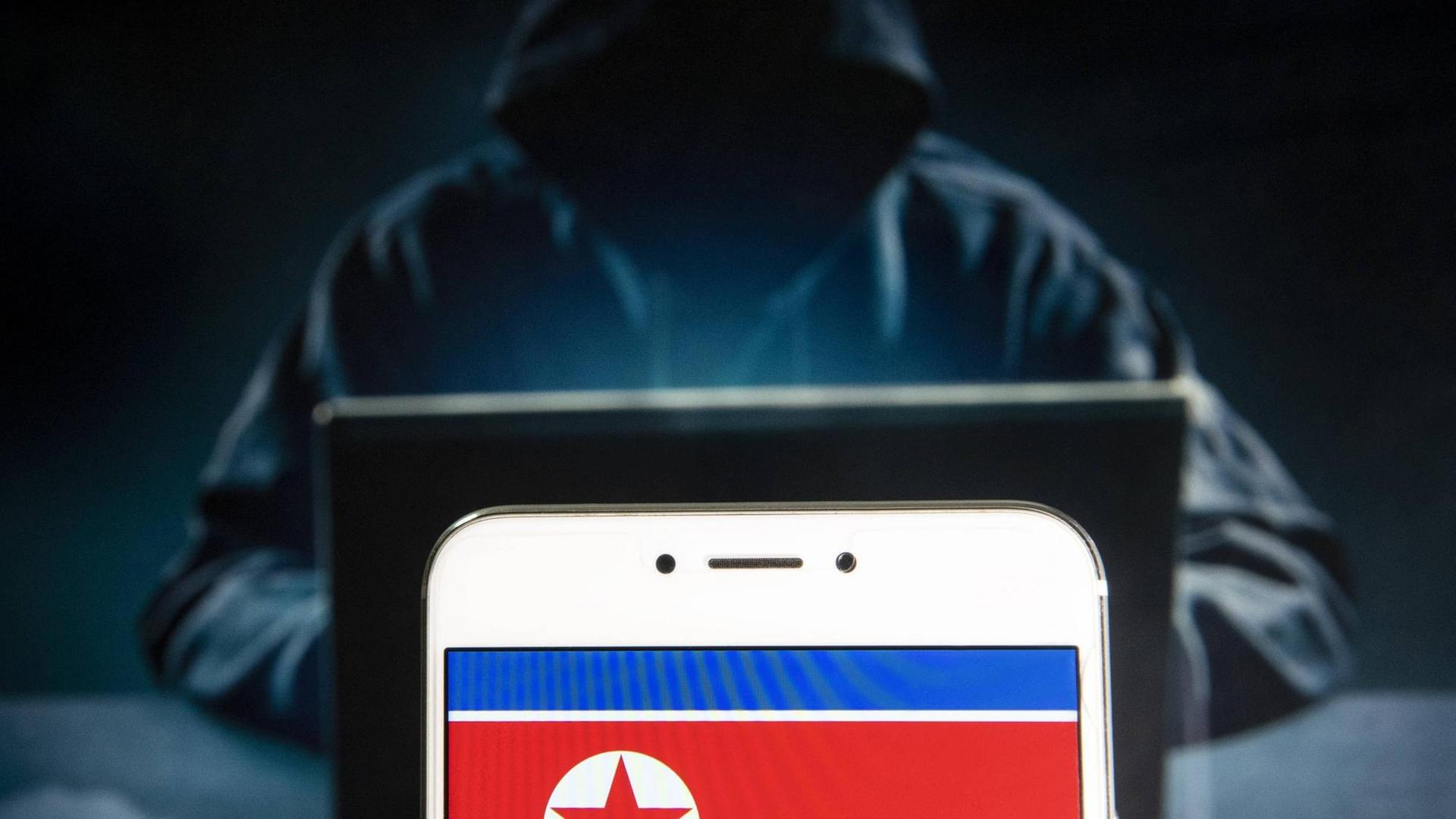 Nordkoreanische Flagge auf Handy vor dunkler Hacker-Gestalt im Kapuzenpulli Nordkoreanische Flagge auf Handy vor dunkler Hacker-Gestalt im Kapuzenpulli