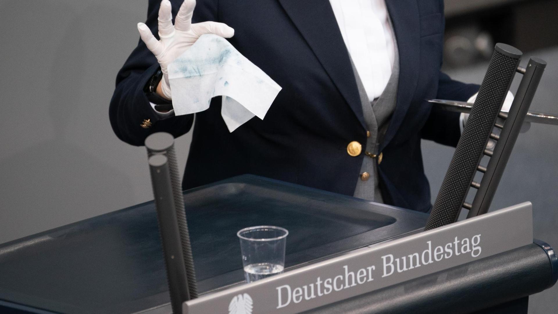 Eine Saaldienerin wischt das Redepult im Bundestag mit Desinfektionsmittel ab.