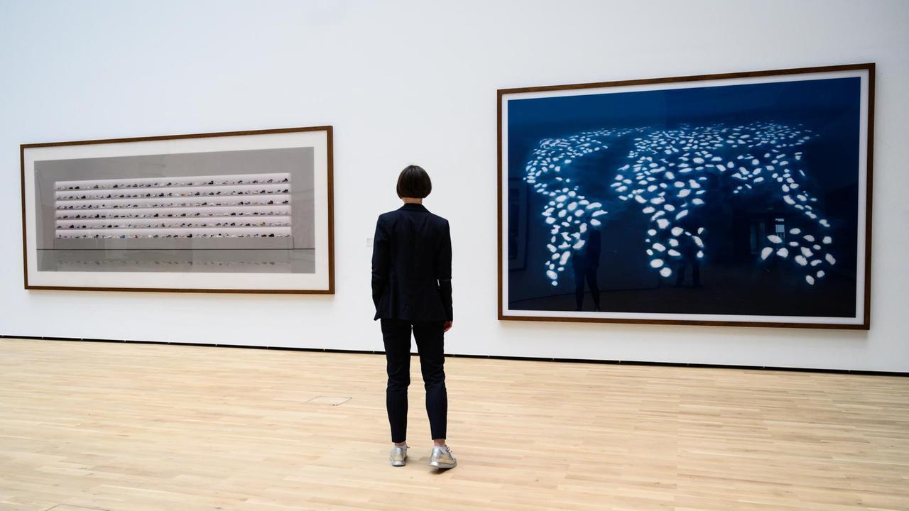 Eine Frau schaut sich die Kunstwerke "Ohne Titel V" (1997) und "Dubai World III" (2008) des Künstlers Andreas Gursky im Kunstmuseum Wolfsburg in der Ausstellung "Now is the time" an.