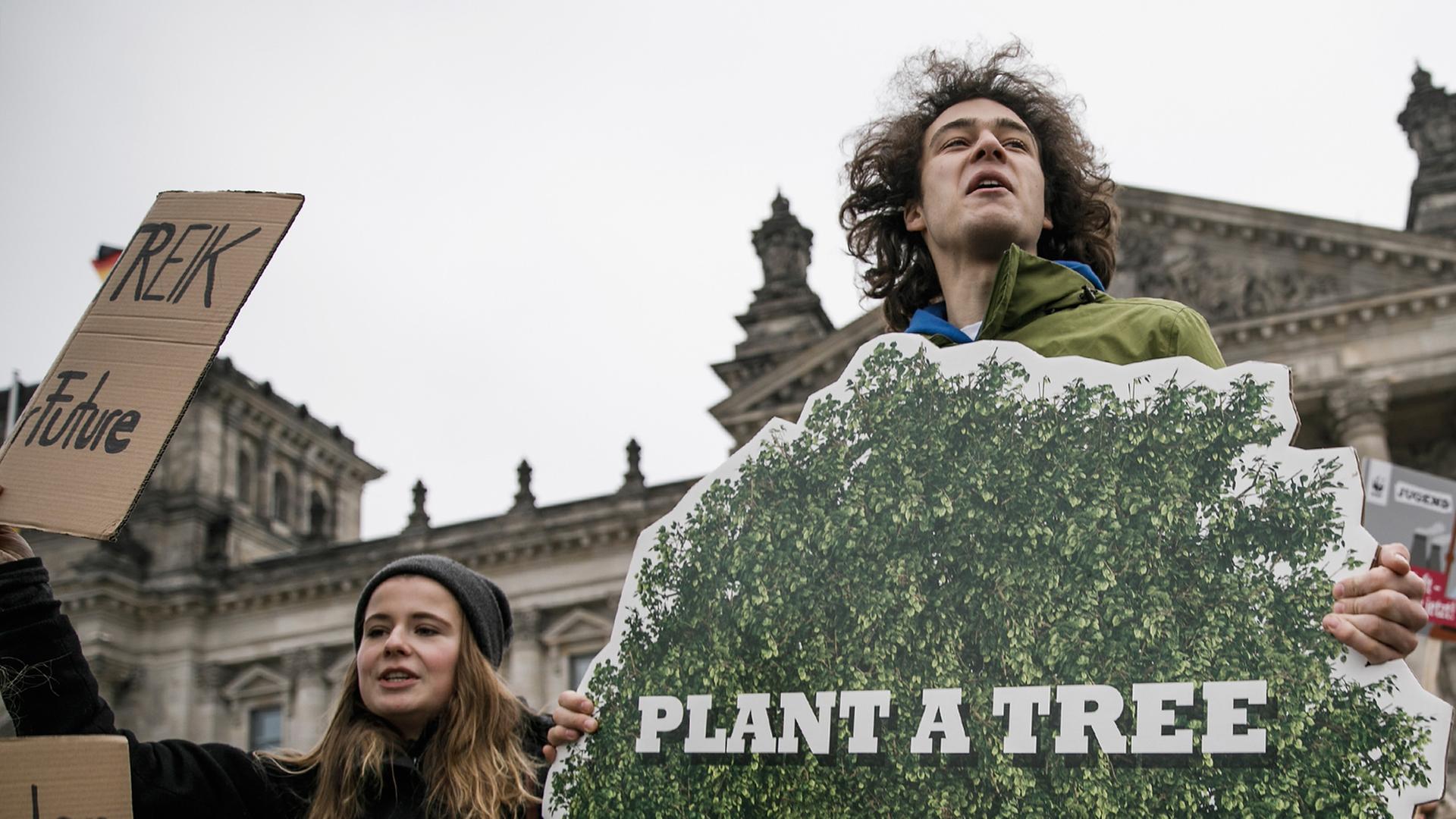Ein junger Mann steht vor dem Bundestag und hält ein Plakat hoch, auf dem steht: "Plant a tree" Ein junger Mann steht vor dem Bundestag und hält ein Plakat hoch, auf dem steht: "Plant a tree"