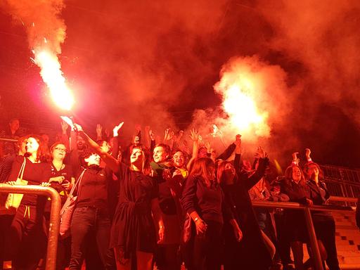 Weibliche Ultrafans aus ganz Europa zur Eröffnung der Ausstellung "Fan.Tastic Females". Eine Gruppe Frauen steht in einem Fußballstadion, das durch Feuer beleuchtet wird.