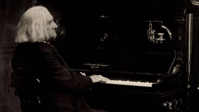 Fotographie des Komponisten, der an einem Klavier sitzt.