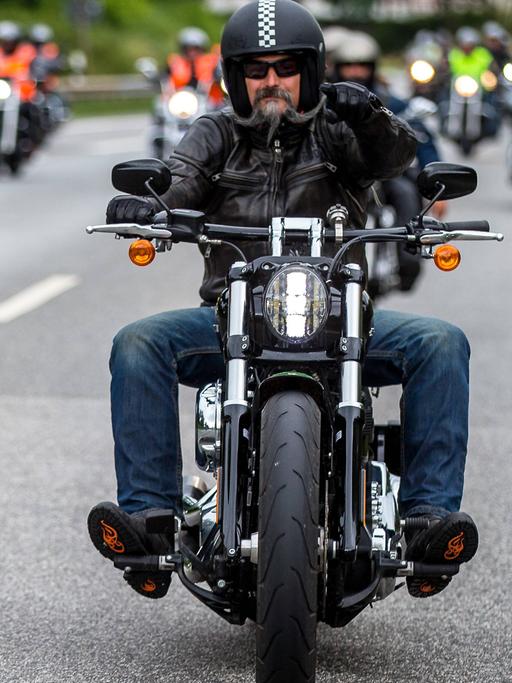 Auf dem Foto fahren zahlreiche Harley Davidson-Fahrer auf den Fotografen zu. Im Vordergrund ist ein Fahrer mit einem gezwirbelten grauen Backenbart im Gesicht.