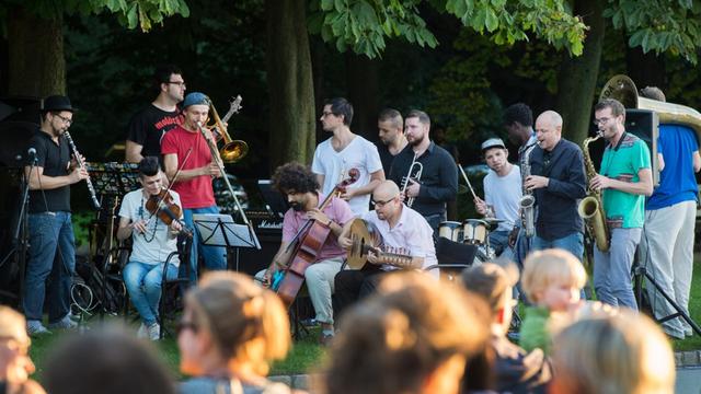 Ewa ein dutzend Männer spielen Blasinstrumente vor Publikum in einem Park.