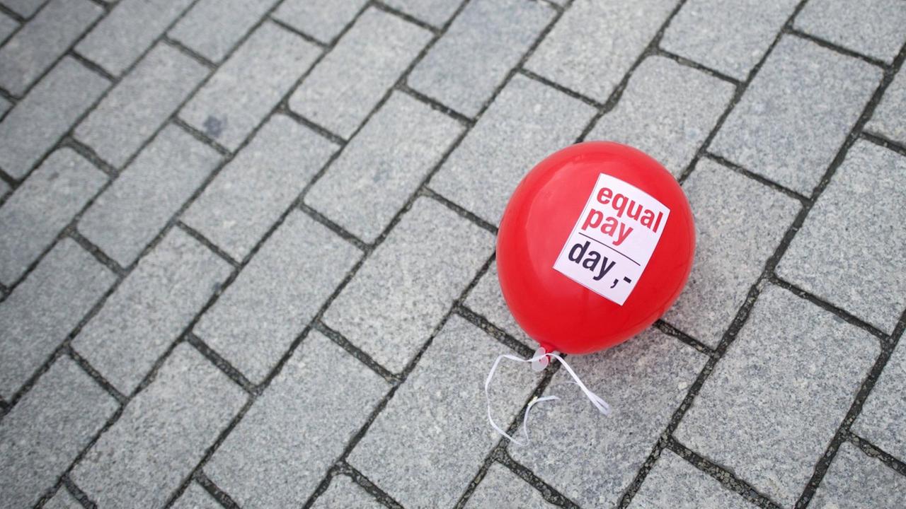 Luftballon mit der Aufschrift "Equal Pay Day" liegt auf Straßenpflaster