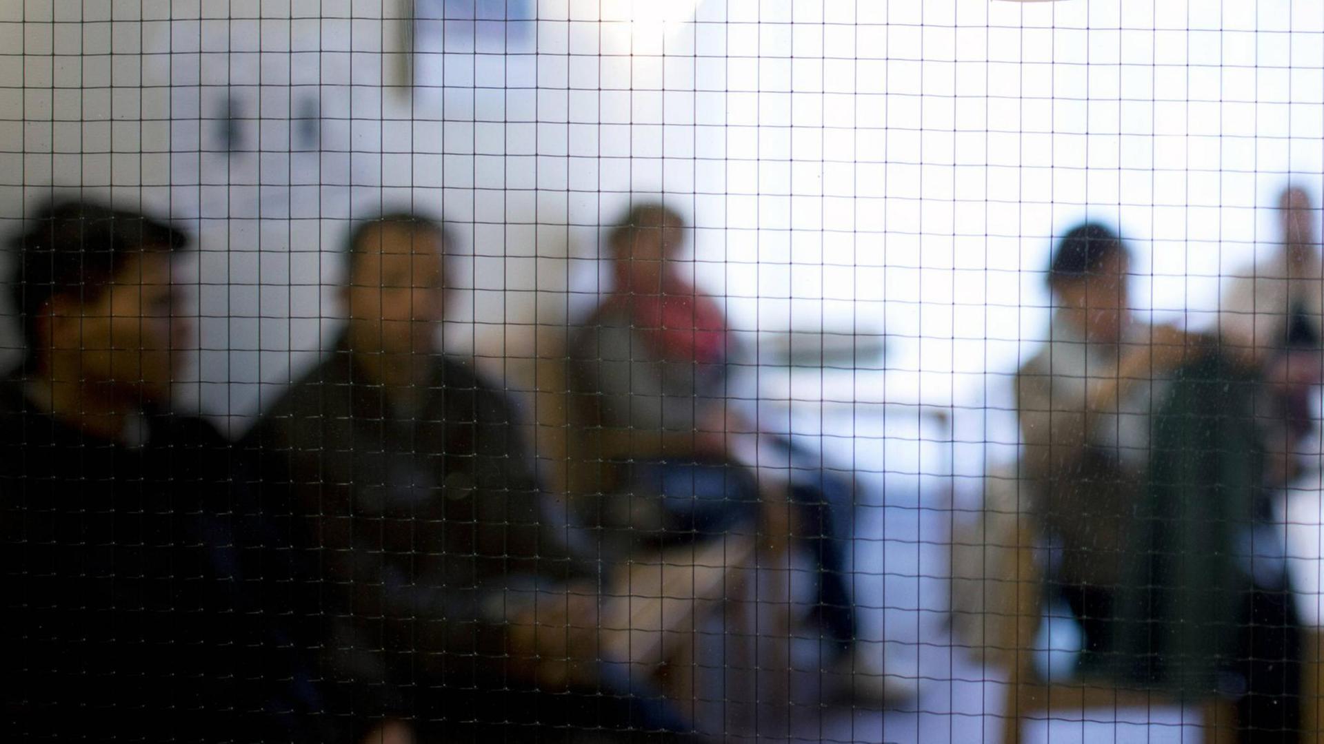 Hinter einer Glasscheibe sind unscharf Menschen zu sehen, die in einem Wartezimmer sitzen. Hinter einer Glasscheibe sind unscharf Menschen zu sehen, die in einem Wartezimmer sitzen.
