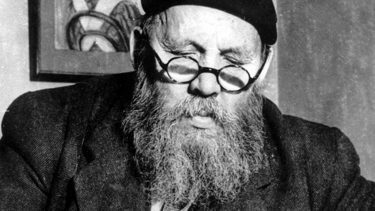 Ein älterer Herr mit Vollbart und Brille sitzt an einem Tisch und schreibt. Ein älterer Herr mit Vollbart und Brille sitzt an einem Tisch und schreibt.