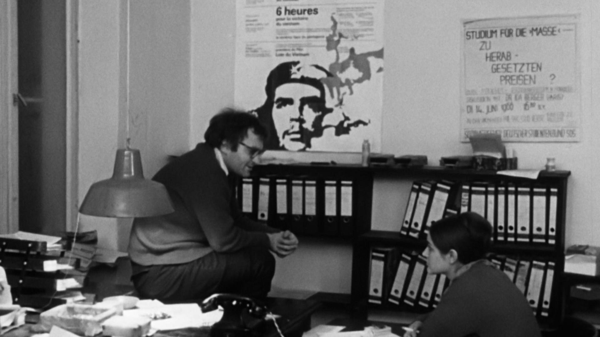 Filmstill aus "Ein Western für den SDS" - Christian Semler und Elke Edelmann in einem Büro, an der Wand hängt ein Poster von Che Guevara