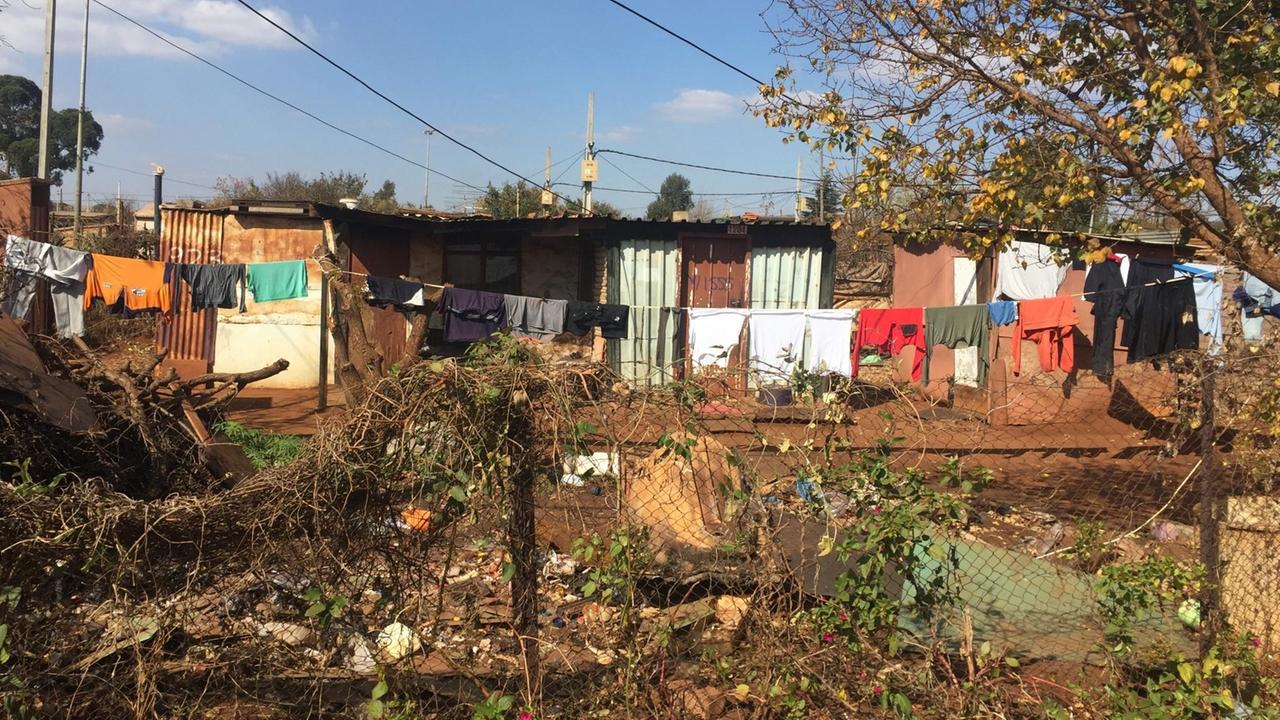 Alltag im Township: Blechhütten, davor Wäsche, die zum Trocknen hängt. Im Vordergrund Müll und Gestrüpp.