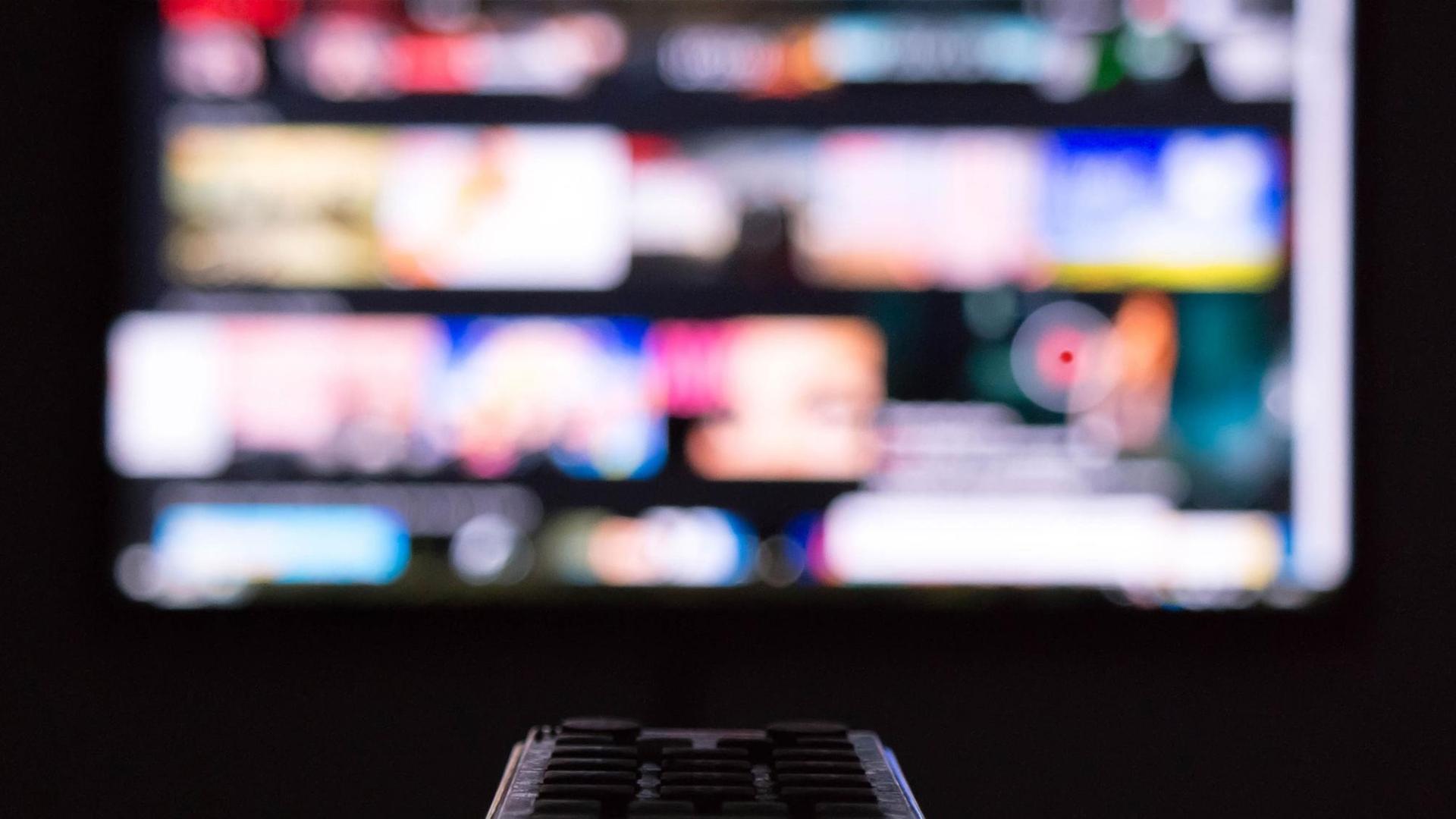 Eine Person sitzt vor einem TV-Monitor und hat die Fernbedienung in der Hand. Eine Person sitzt vor einem TV-Monitor und hat die Fernbedienung in der Hand.