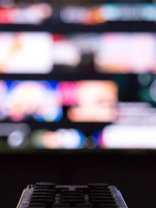 Eine Person sitzt vor einem TV-Monitor und hat die Fernbedienung in der Hand.