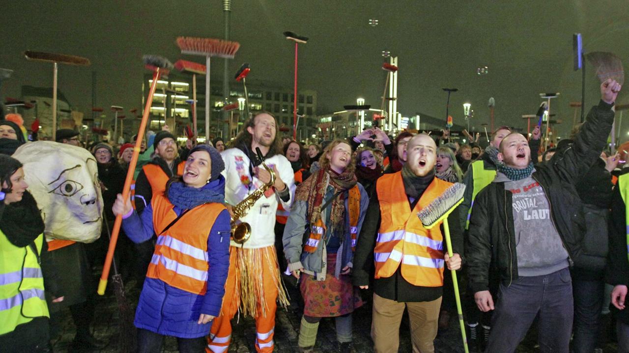Anti-Pegida-Demonstranten in Dresden mit Warnwesten und Besen. Dresdner Künstler fegten am 5. Januar 2015 mit einem Kehraus - einem Neujahrsputz - den Platz der Pegida-Kundgebung symbolisch sauber. Anti-Pegida-Demonstranten in Dresden mit Warnwesten und Besen. Dresdner Künstler fegten am 5. Januar 2015 mit einem Kehraus - einem Neujahrsputz - den Platz der Pegida-Kundgebung symbolisch sauber.