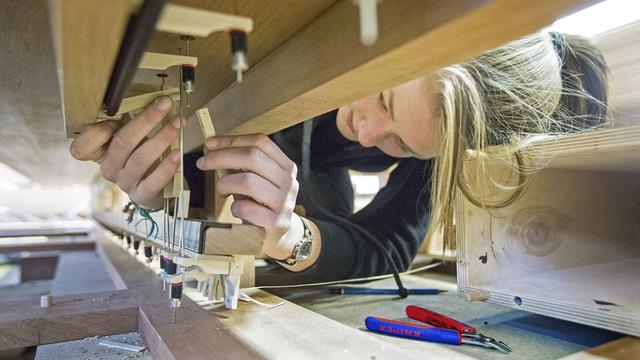 Eine junge Frau arbeitet an einem Orgel-Spieltisch in einer Orgelwerkstatt.