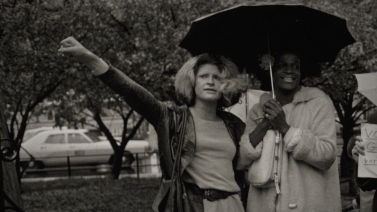 Schwarz-Weiß-Aufnahme von den zwei LGBTQ-Aktivistinnen Sylvia Rivera und Marsha Johnson vor einer Polizeiabsperrung. Schwarz-Weiß-Aufnahme von den zwei LGBTQ-Aktivistinnen Sylvia Rivera und Marsha Johnson vor einer Polizeiabsperrung.