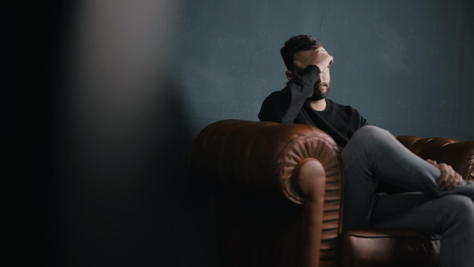 Ein Mann sitzt traurig auf einem Sofa und hält die Hand vor sein Gesicht. Ein Mann sitzt traurig auf einem Sofa und hält die Hand vor sein Gesicht.