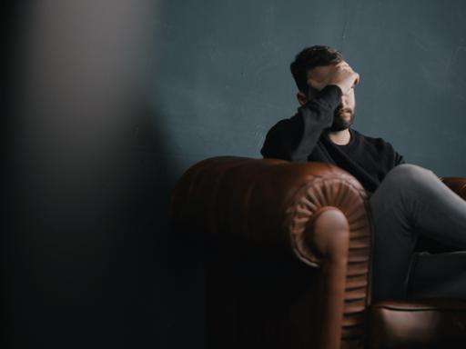 Ein Mann sitzt traurig auf einem Sofa und hält die Hand vor sein Gesicht