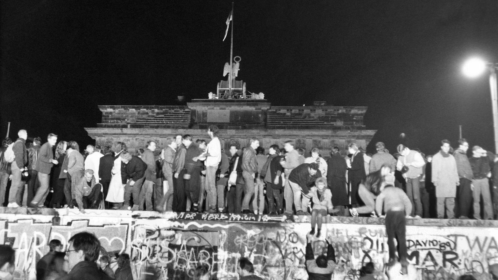 9. November 1989, Menschen stehen auf der Berliner Mauer vor dem Brandenburger Tor und feiern den Mauerfall 9. November 1989, Menschen stehen auf der Berliner Mauer vor dem Brandenburger Tor und feiern den Mauerfall