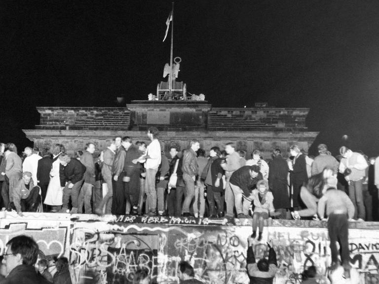 9. November 1989, Menschen stehen auf der Berliner Mauer vor dem Brandenburger Tor und feiern den Mauerfall