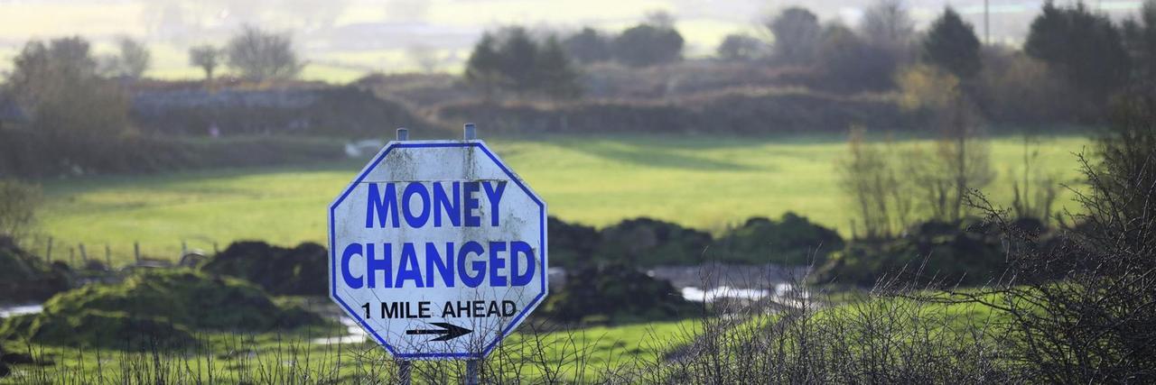 Ein Straßenschild mit der Aufschrift "Money Changed" (Geld wechseln) steht in einer Hecke an der Grenze zwischen Nordirland und der Republik Irland. Ein Straßenschild mit der Aufschrift "Money Changed" (Geld wechseln) steht in einer Hecke an der Grenze zwischen Nordirland und der Republik Irland.