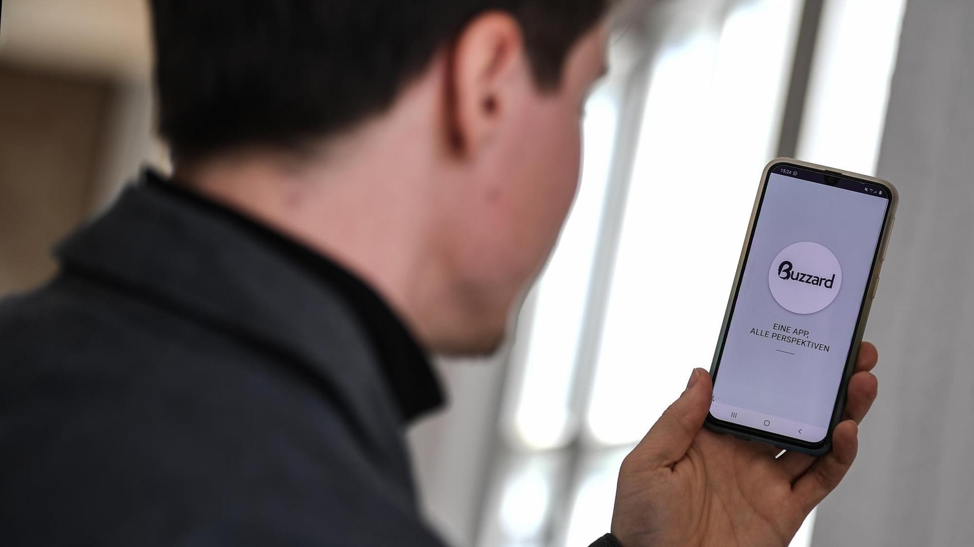 Ein Mann blickt auf sein Smartphone, auf dem die App "The Buzzard" geöffnet ist. Ein Mann blickt auf sein Smartphone, auf dem die App "The Buzzard" geöffnet ist.