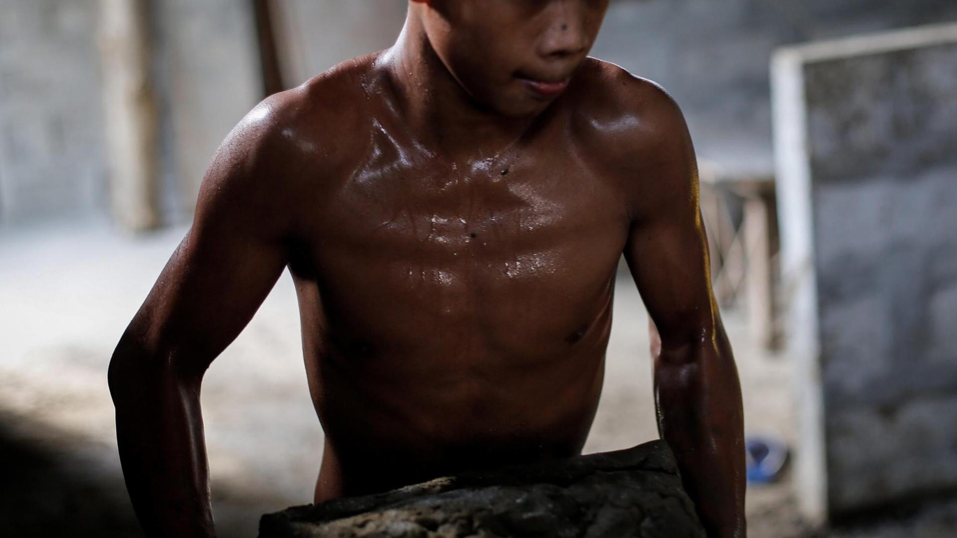 Ein philippinischer Junge trägt schwitzend mit freiem Oberkörper in einer Keramikfabrik schweren Lehm