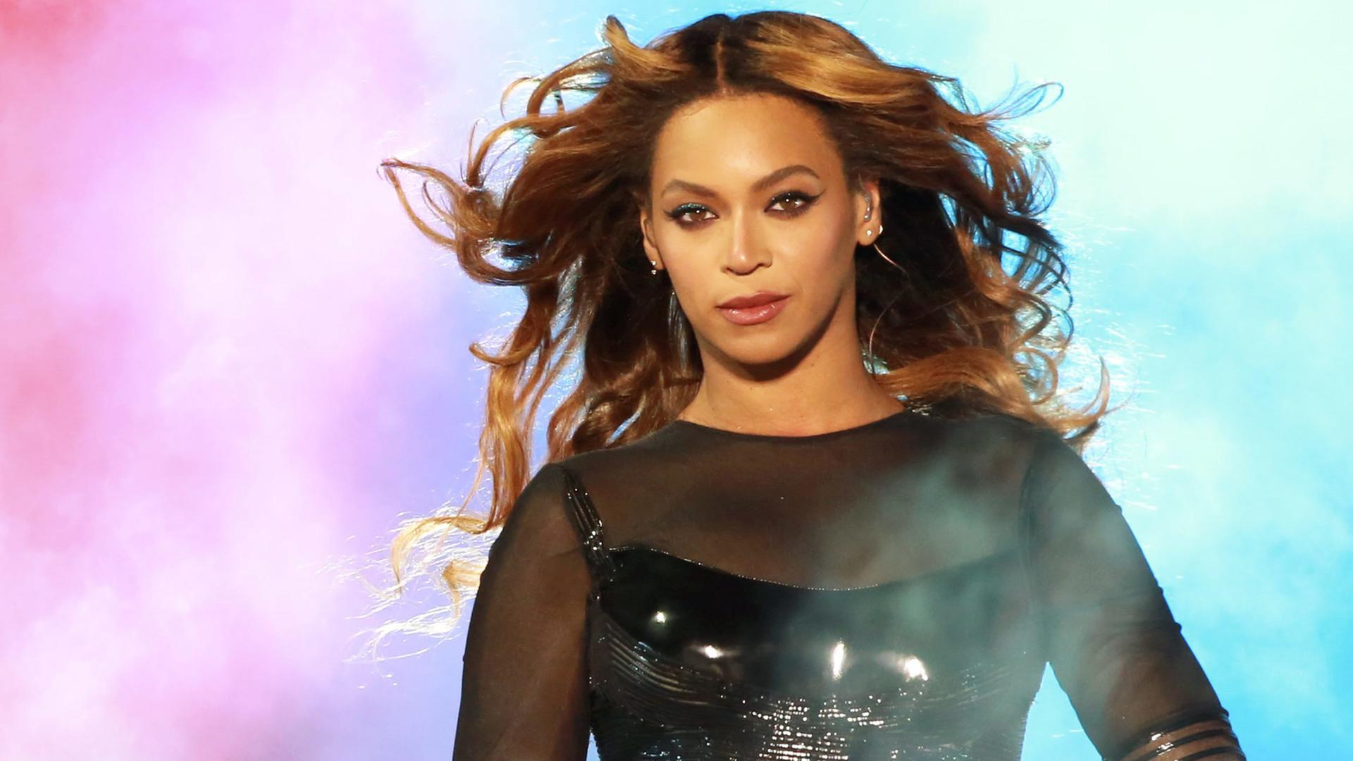 Die amerikanische Musikerin Beyoncé steht bei einem Auftritt im Jahr 2014 mit einem Mikrofon in der Hand auf einer Bühne, hinter ihr Nebel in verschiedenen Farben. Die amerikanische Musikerin Beyoncé steht bei einem Auftritt im Jahr 2014 mit einem Mikrofon in der Hand auf einer Bühne, hinter ihr Nebel in verschiedenen Farben.