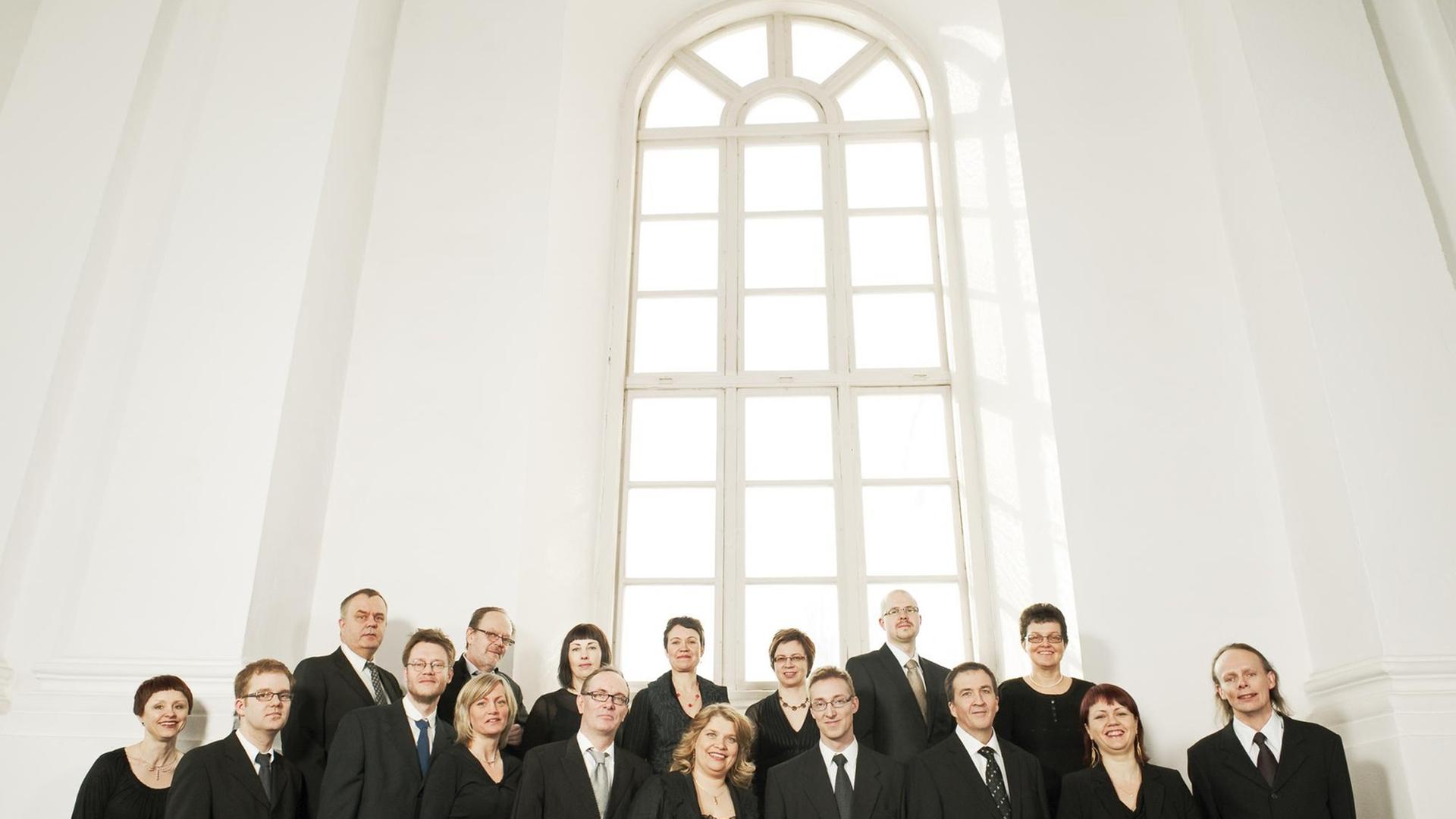 Der Chor steht in einem hellen Raum vor einem hohen Kirchenfenster. Der Chor steht in einem hellen Raum vor einem hohen Kirchenfenster.
