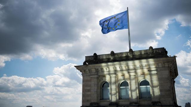 Eine Europaflagge weht am 06.07.2015 auf dem Dach des Deutschen Bundestages, dem Reichstagsgebäude, in Berlin vor dunklen Wolken.