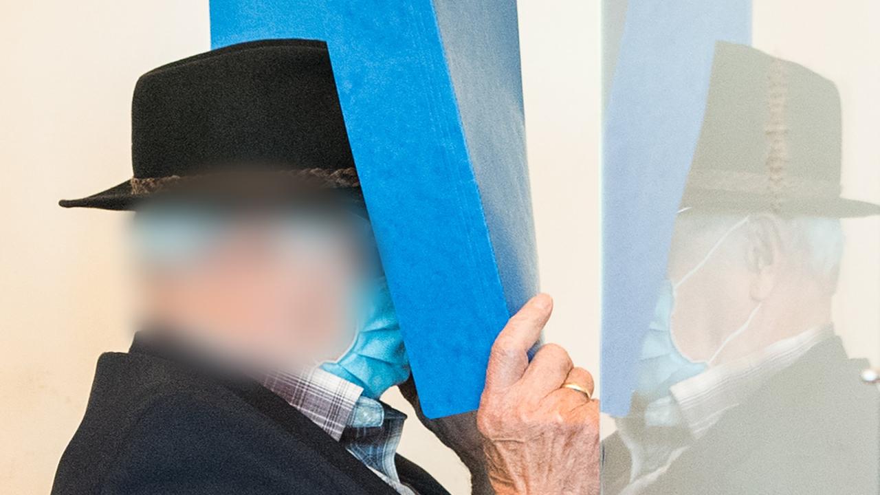 Ein Mann mit Hut hält sich eine Akte vor das Gesicht. Ein Mann mit Hut hält sich eine Akte vor das Gesicht.