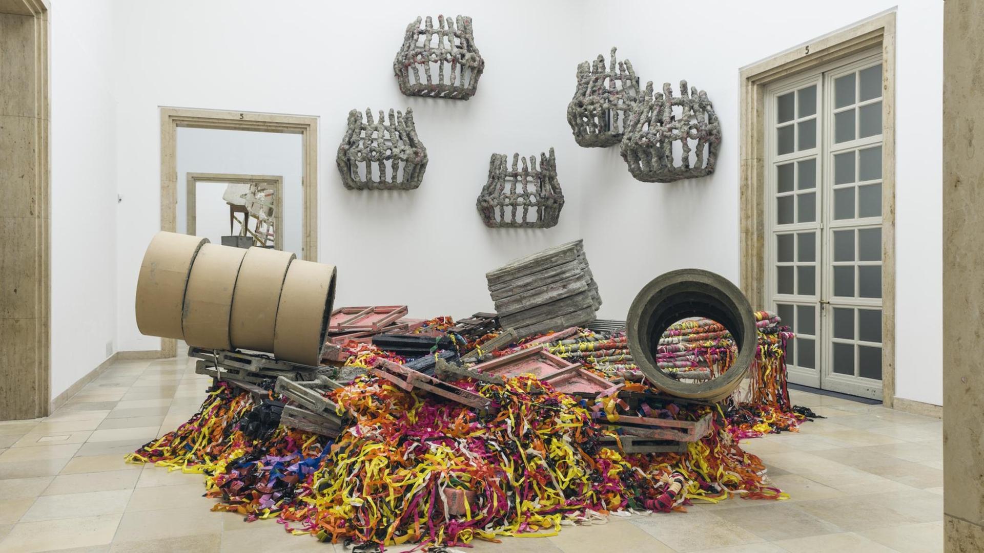 Installationsansicht der Skulptur-Ausstellung von Phyllida Barlow im Haus der Kunst in München. Die namenlose Skulptur besteht aus einem Wust aus bunten, breiten lametterartigen Streifen, dazwischen in Obstkisten ähnliche Holzpaletten und oberdrauf in Scheiben geschnittene, wieder zusammengesetzte Röhren-Ringe. Installationsansicht der Skulptur-Ausstellung von Phyllida Barlow im Haus der Kunst in München. Die namenlose Skulptur besteht aus einem Wust aus bunten, breiten lametterartigen Streifen, dazwischen in Obstkisten ähnliche Holzpaletten und oberdrauf in Scheiben geschnittene, wieder zusammengesetzte Röhren-Ringe.
