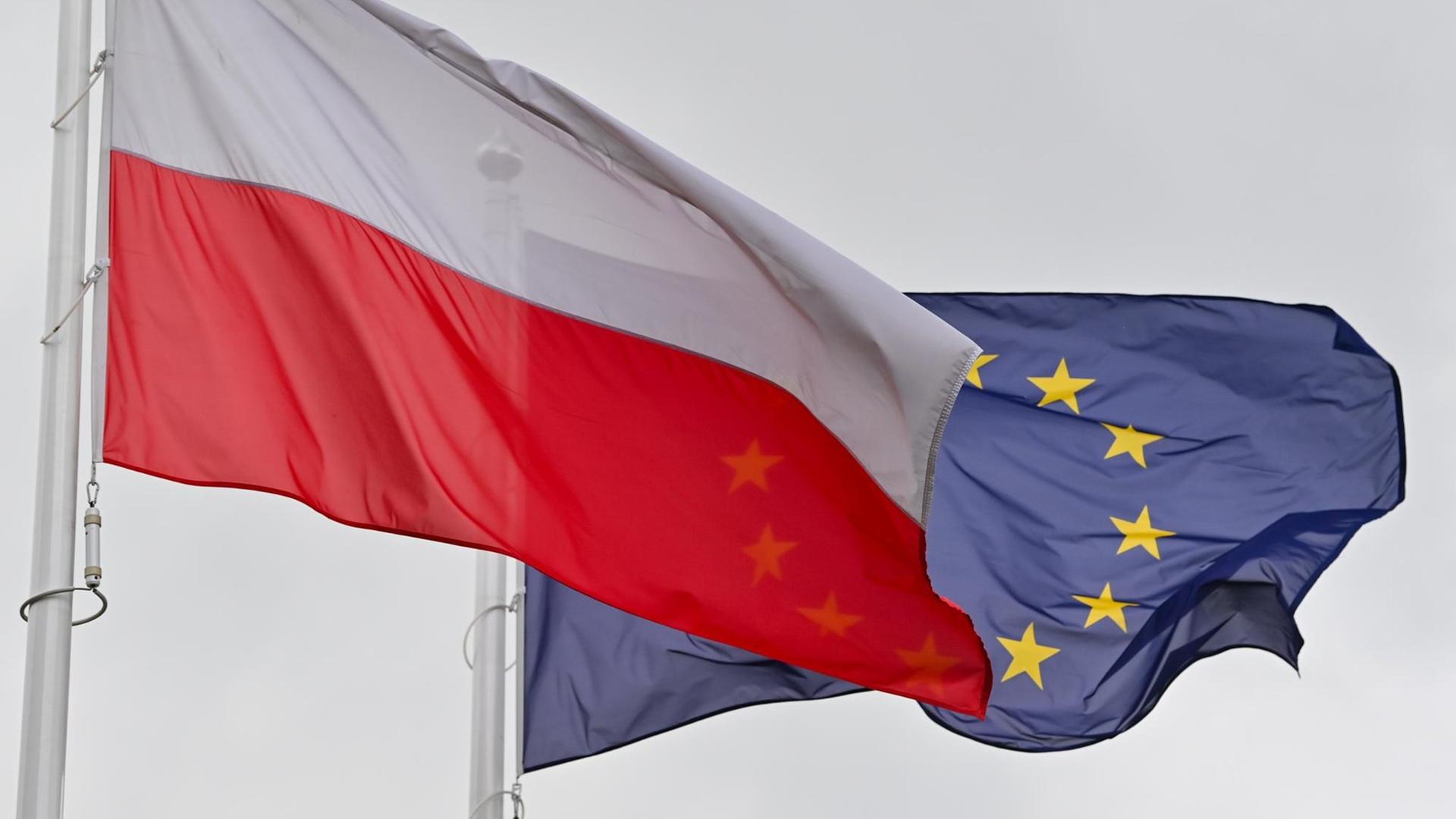 Die weiß-rote Nationalfahne Polens und dahinter die Fahne der Europäischen Union (EU) wehen im Wind. Die weiß-rote Nationalfahne Polens und dahinter die Fahne der Europäischen Union (EU) wehen im Wind.