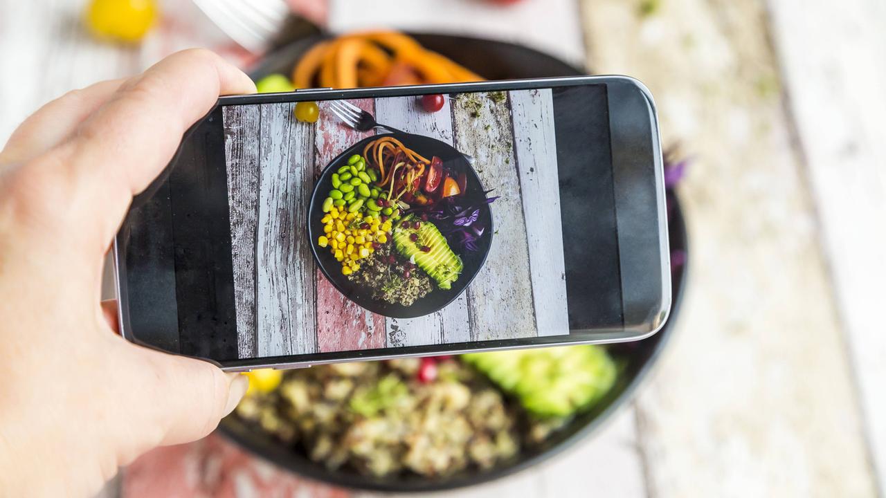 Eine Frau fotografiert ihre vegane Lunch bowl mit ihrem Smartphone. Eine Frau fotografiert ihre vegane Lunch bowl mit ihrem Smartphone.