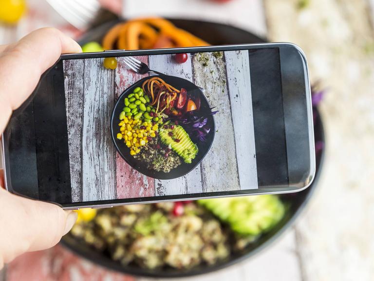 Eine Frau fotografiert ihre vegane Lunch bowl mit ihrem Smartphone.