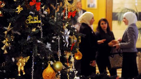 Ein Weihnachtsbaum im syrischen Damaskus. Im Hintergrund sieht man drei Frauen, die sich unterhalten. Zwei von ihnen tragen weiße Kopftücher.