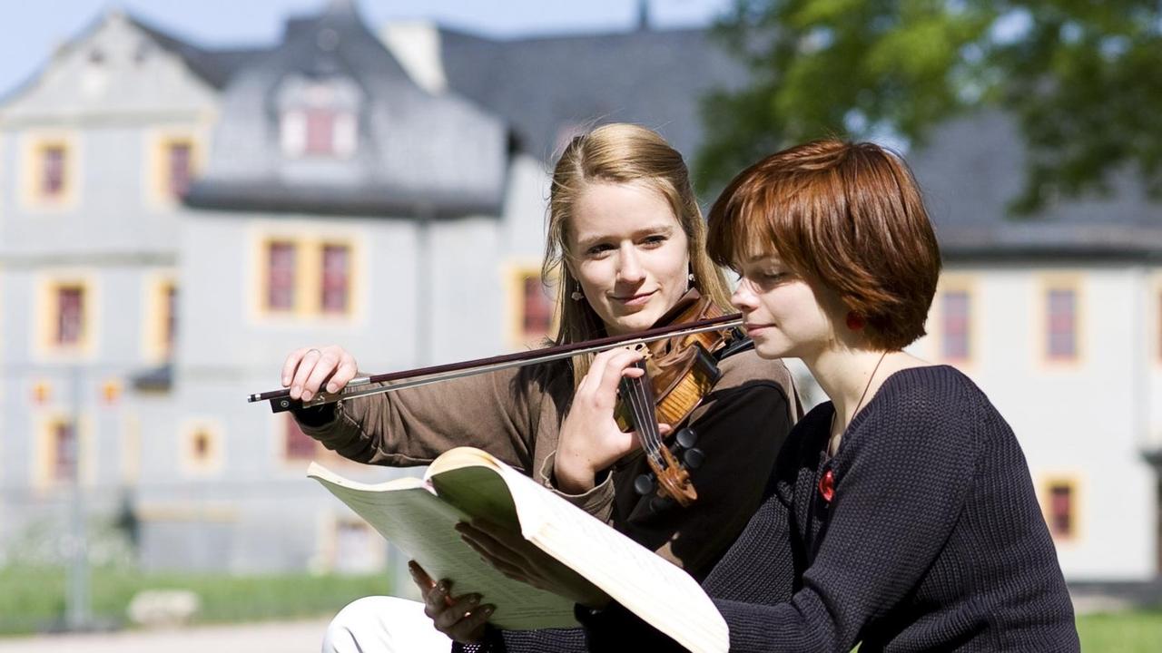 Eine Geigerin sitzt mit einer Freundin übend im Park vor dem Renaissance-Teil des Weimarer Schlosses. Eine Geigerin sitzt mit einer Freundin übend im Park vor dem Renaissance-Teil des Weimarer Schlosses.