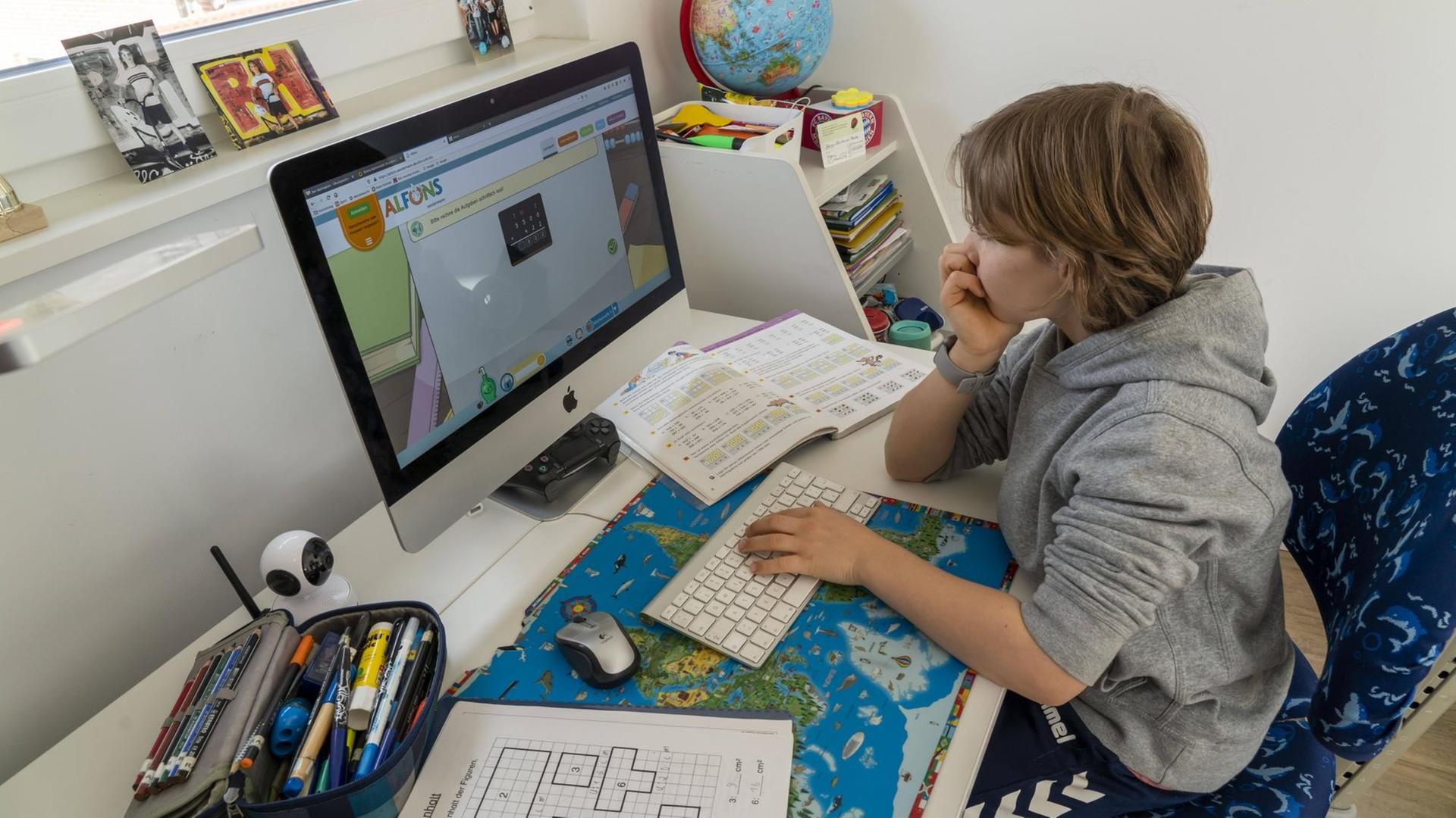 Ein Junge sitzt zu Hause an seinem Schreibtisch vor dem Computer und lernt Ein Junge sitzt zu Hause an seinem Schreibtisch vor dem Computer und lernt