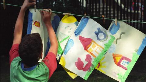 Ein Kind hängt selbstgezeichnete Bilder an einer Wäscheleine auf.