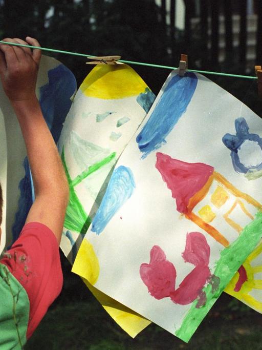 Ein Kind hängt selbstgezeichnete Bilder an einer Wäscheleine auf.
