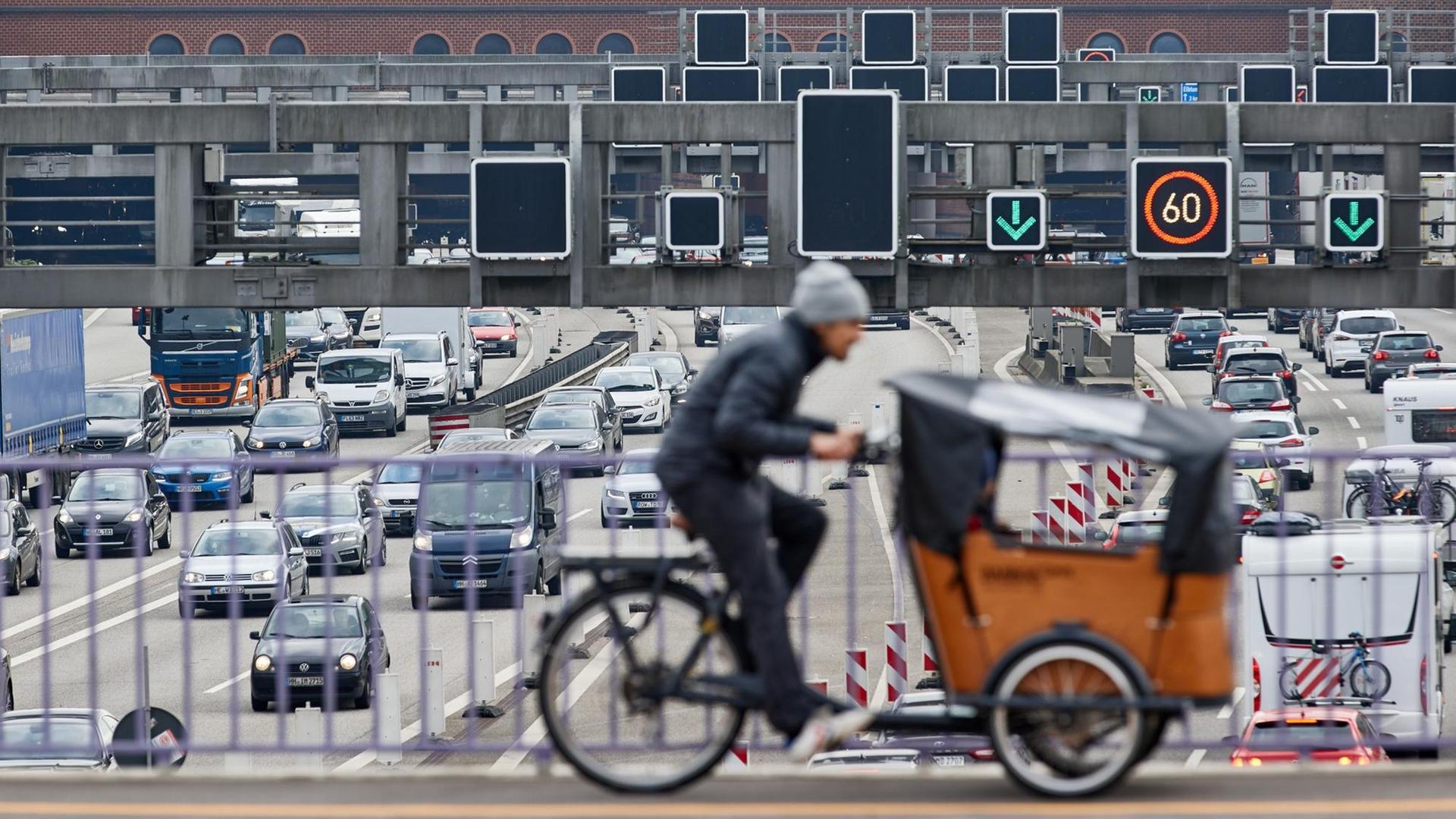 Ein Lastenrad-Fahrer fährt über die Brücke Behringstraße über die Autobahn 7, auf der sich vor dem Elbtunnel der Verkehr staut. Ein Lastenrad-Fahrer fährt über die Brücke Behringstraße über die Autobahn 7, auf der sich vor dem Elbtunnel der Verkehr staut.