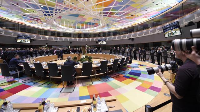 Ein Blick auf den beginnenden EU-Gipfel: Man sieht den runden Tisch und bunte Farben auf dem Boden und an der Decke.