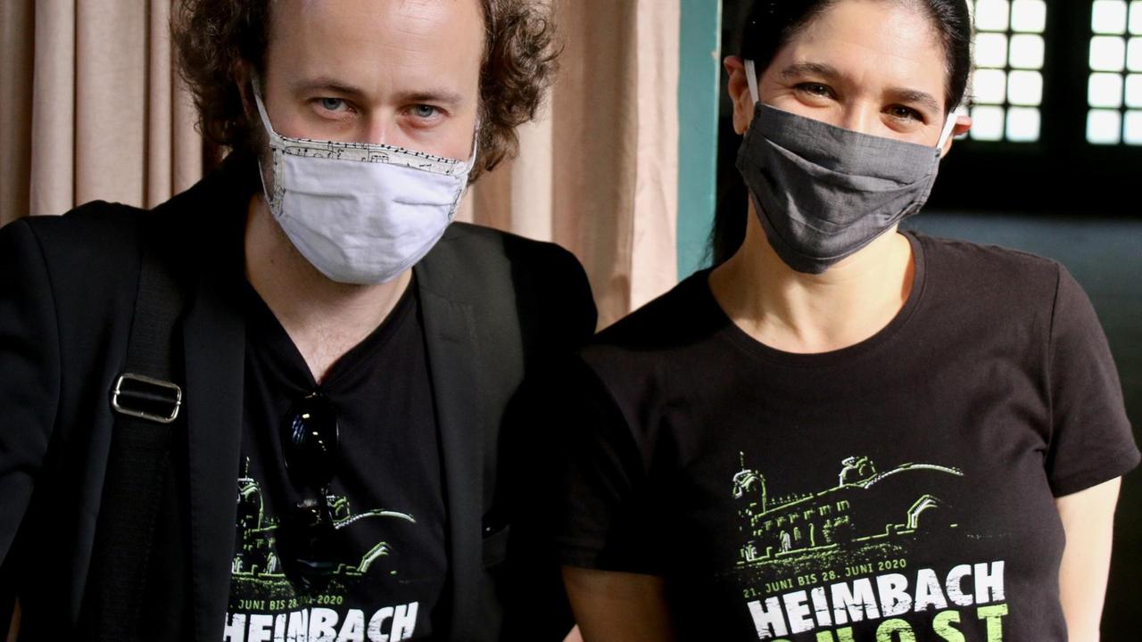 Mann und Frau mit Mundschutz tragen T-Shirts mit dem Aufdruck "Heimbach Ghost". Mann und Frau mit Mundschutz tragen T-Shirts mit dem Aufdruck "Heimbach Ghost".
