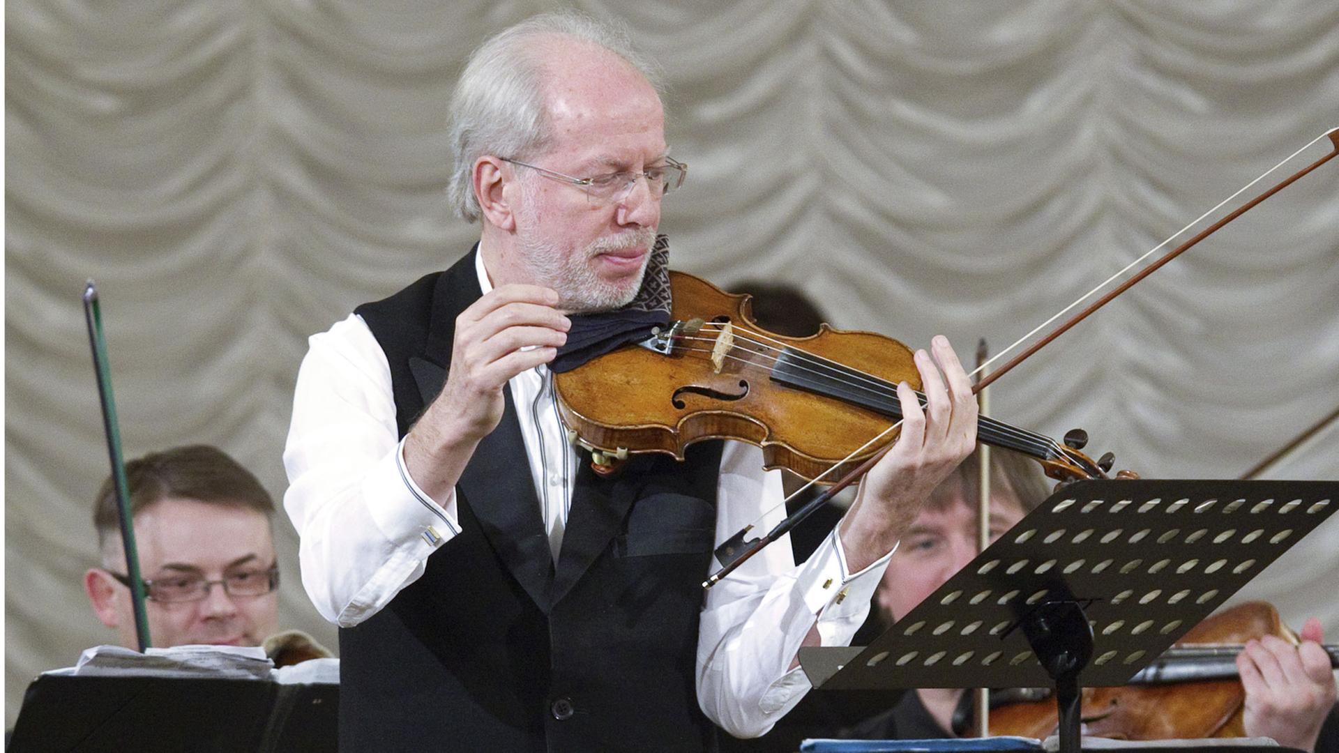 Der Geiger Gidon Kremer bei einem Auftritt mit dem Orchester Kremerata Baltica. Aufgenommen wurde das Bild in der Columns Hall während des Mstislav Rostropovich International Festival. Kremer hat die Violine im linken Arm eingeklemmt, dort befindet sich auch noch der Bogen. Vor ihm ist ein Notenständer aufgebaut. Im Hintergrund sind einige Musiker zu sehen. Der Geiger Gidon Kremer bei einem Auftritt mit dem Orchester Kremerata Baltica. Aufgenommen wurde das Bild in der Columns Hall während des Mstislav Rostropovich International Festival. Kremer hat die Violine im linken Arm eingeklemmt, dort befindet sich auch noch der Bogen. Vor ihm ist ein Notenständer aufgebaut. Im Hintergrund sind einige Musiker zu sehen.