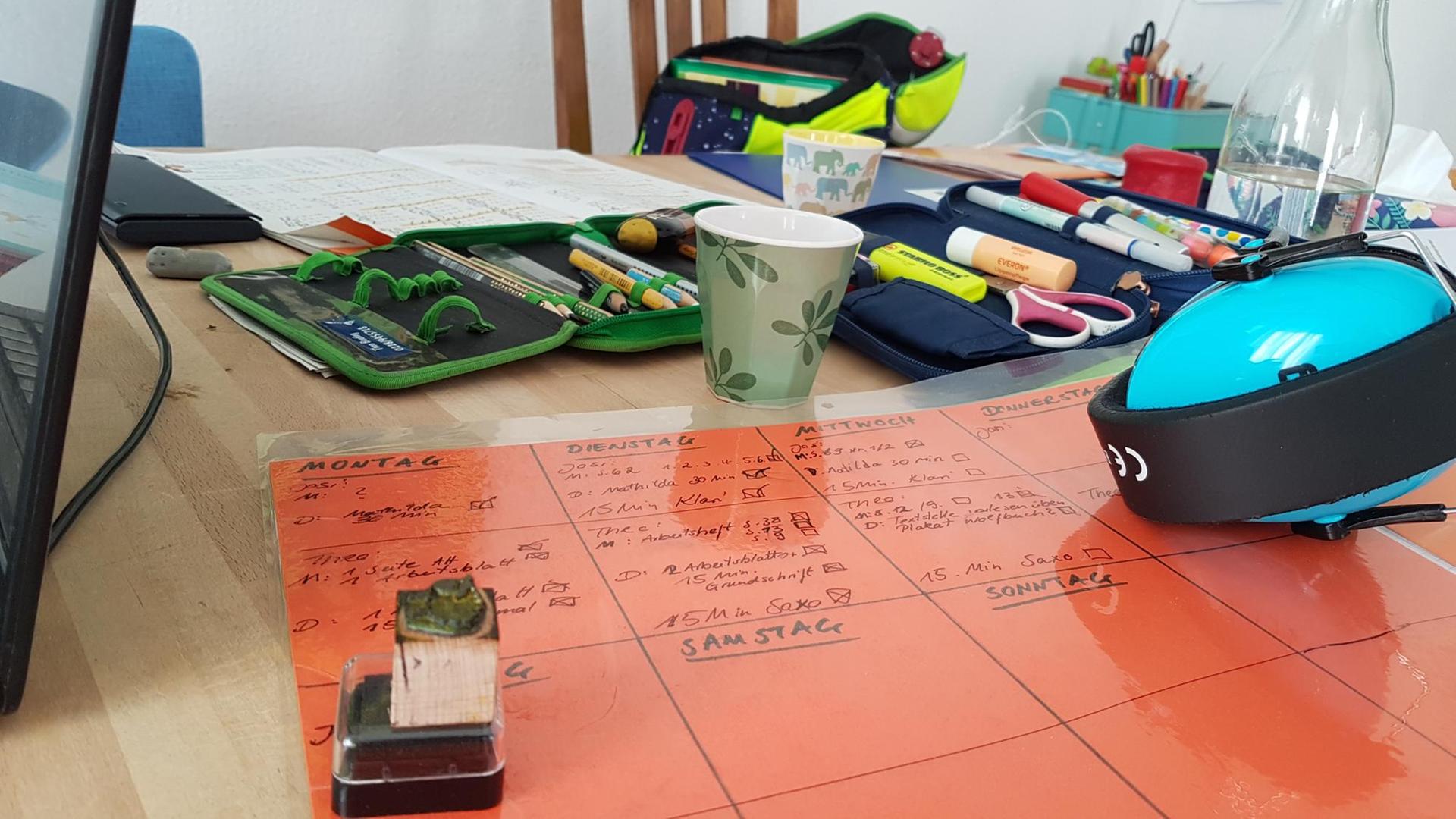 Ein Tisch mit aufgeklappten Federmäppchen, einem Stundenplan, Schreibutensilien und Bechern. Ein Tisch mit aufgeklappten Federmäppchen, einem Stundenplan, Schreibutensilien und Bechern.