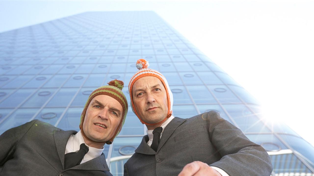 Die Künstler Ulan und Bator tragen Strickmützen und stehen vor einem Hochhaus. Die Künstler Ulan und Bator tragen Strickmützen und stehen vor einem Hochhaus.