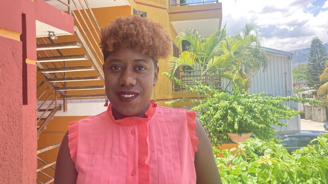 Eine Frau in pink und toupierter Frisur steht vor einem pink Haus. Im Hintergrund Palmen. Eine Frau in pink und toupierter Frisur steht vor einem pink Haus. Im Hintergrund Palmen.