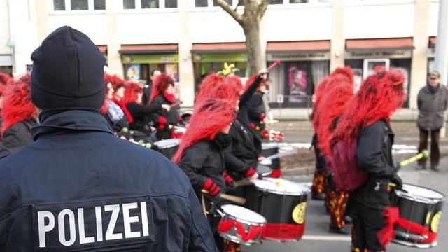 Ein Polizist steht beim Karnevalsumzug in Braunschweig, während verkleidete Narren an ihm vorbeiziehen, aufgenommen am 10.02.2013.