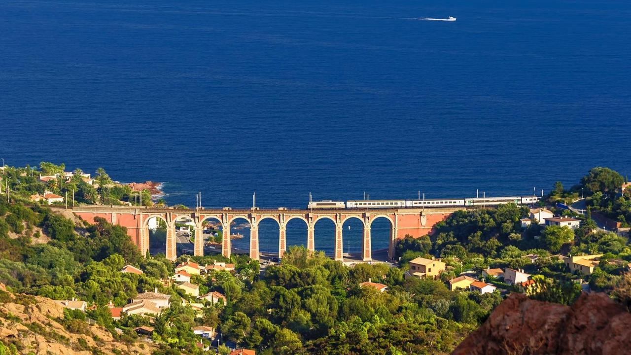 Ein Zug fährt in Südfrankreich entlang der Küste über ein altes Viadukt mit direktem Blick auf das offene Meer.