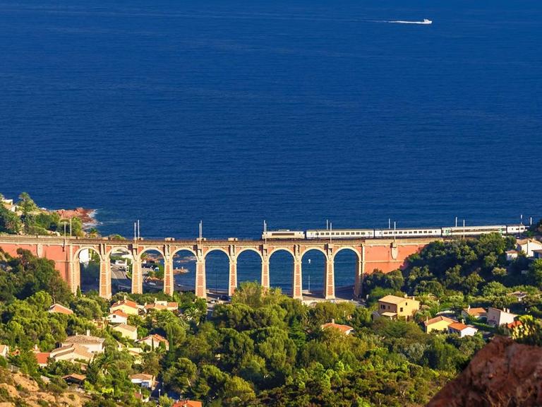 Ein Zug fährt in Südfrankreich entlang der Küste über ein altes Viadukt mit direktem Blick auf das offene Meer.