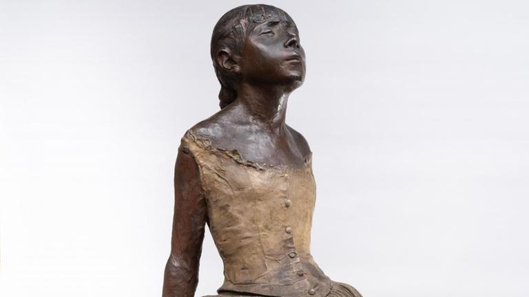 Eine Mädchen-Skulptur im Tanzrock verschränkt die Arme hinter dem Rücken.